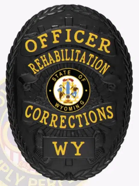 Oval-shaped black metal badge with gold letters reading "Officer Rehabilitation Corrections WY." The center displays the official Wyoming state seal, and the badge is equipped with a safety pin for secure attachment.