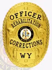 Custom Wyoming Rehabilitation Corrections officer badge in gold metal, oval shaped with detailed laurel border, bold black lettering, and a central State of Wyoming seal, designed for official law enforcement use with a safety pin attachment.