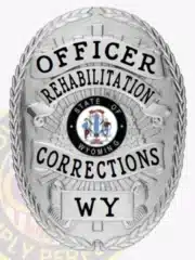 Custom silver oval metal badge with black lettering for an Officer in Rehabilitation Corrections, Wyoming. The badge features the Wyoming state seal prominently in the center and includes a safety pin attachment on the back.