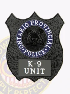 Close-up of a custom black shield metal badge for ontario provincial police k-9 unit, displaying the official crest and clear 'k-9 unit' label, attached with a safety pin.