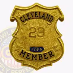 Custom gold shield metal badge for fraternal order of police cleveland member, featuring a textured gold surface with embossed number "23" in the center, black text reading "cleveland" at the top and "member" at the bottom, with a small blue f. O. P. A. Emblem in the middle, secured by a safety pin attachment.