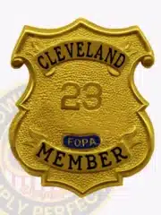 Image showing a custom gold shield metal badge for Fraternal Order of Police Cleveland member with safety pin attachment, featuring the embossed number 23, black text on banners reading “CLEVELAND” and “MEMBER,” and a blue F.O.P.A. emblem on a textured gold badge