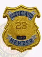 Image showing a custom gold shield metal badge with silver panels for Fraternal Order of Police Cleveland member, highlighting the detailed textured gold surface, silver banners with blue text, prominent number "23," and a safety pin backing for secure wear.