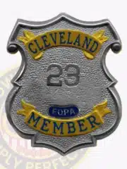 Detailed image of a custom silver shield metal badge designed for the Fraternal Order of Police Cleveland member, showcasing smooth silver edges, gold decorative panels with embossed lettering, and a safety pin attachment on the back for easy mounting.