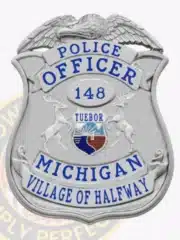 Silver shield-shaped police badge for Village of Halfway, Michigan, with eagle top design, colored Michigan state seal in the center, identification number 148, and safety pin on the back.