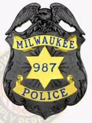 Custom Milwaukee Police badge featuring a black top shield design with a detailed eagle perched on top, gold star in the center displaying badge number 987, and gold banners with blue lettering reading "MILWAUKEE" and "POLICE," attached by a safety pin.