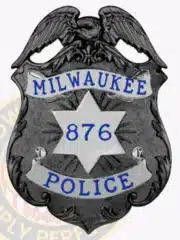 Black eagle top shield badge for Milwaukee Police Department, silver panels highlighting the text 'MILWAUKEE POLICE' and star-shaped center with number 876, equipped with safety pin on the back.