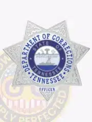 Polished custom silver 7-point star metal badge for Tennessee Department of Corrections, featuring embossed decorative details, central state seal with agricultural imagery, surrounded by blue text identifying the department, and an "OFFICER" label beneath; attached with a safety pin.